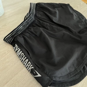 Svarta löparshorts - Svarta löparshorts från Gymshark med snygga loggor på sidorna och fickor. Nyskick!