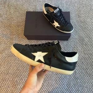 Golden goose - Säljer dessa fräscha svarta Golden goose skor i storlek 43. Skorna är i bra skick 7/10. Lite slitningar på hälarna (bild 3) samt Lädert har släppt lite från sulan (bild 5). Endast skorna ingår. Självklart autentiska. Hör gärna av dig vid frågor😉👊🏽