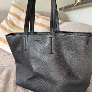 Väska Don Donna - Svart väska i imitationsläder från Don Donna i nyskick.   Material:  Yttre 100% polyuteran Foder 100% polyester   Mått:  Bredd ca 32 cm Höjd ca 27 cm Handtag ca 27 cm