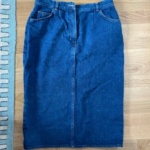 Blå jeanskjol - Mellanlång jeanskjol som går till under knäna. Midwaist med dragkedja och knapp. Köp second hand men är i bra skick.