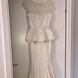 Vit spetsklänning - Helt ny! Otroligt fin klänning ✨En elegant vit långklänning med spetsdetaljer. Klänningen har en peplumdetalj i midjan och är ärmlös med en transparent överdel. Den har en vacker, flödande kjol som ger en klassisk och sofistikerad look.