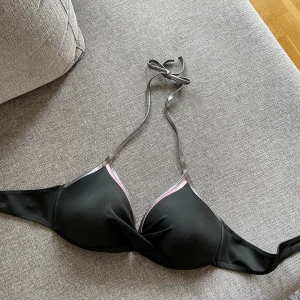 Ny Svart bikiniöverdel - Ny Svart bikiniöverdel med silverfärgade band och rosa detaljer. Överdelen har en push-up-effekt och är justerbar i ryggen. Kupa D. •Aldrig använda bikini-bh med push-up. Endast upptvättade. Etiketten är inte kvar •Köpte på Calzedonia för ungefär 450
