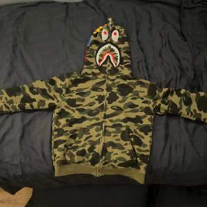 Säljer nu denna Bape hoodie. Den är rätt så använda men har fortfarande mycket liv i sig. Den är 1:1. Den har riktigt snygga detaljer på luvan. Ena fickan är lite trasig. Det är bara att höra av sig vid frågor om hoodien😊😊😊