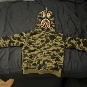 Säljer nu denna Bape hoodie. Den är rätt så använda men har fortfarande mycket liv i sig. Den är 1:1. Den har riktigt snygga detaljer på luvan. Ena fickan är lite trasig. Det är bara att höra av sig vid frågor om hoodien😊😊😊