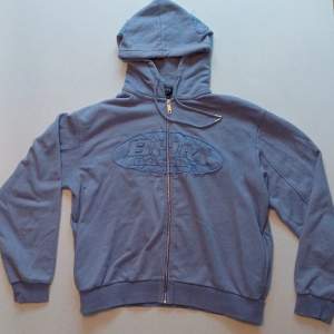 Lila blå zip hoodie med snygga påsydda märken på bröstet och luvan. Oversized passform