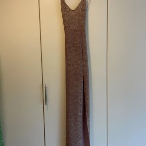 Balklänning  - Lila och guldskimrande balklänning i stretchigt material. Hög slits, tunna axelband som korsas i ryggen. Några trådar har gått upp i ryggen men det är inget som syns tydligt (se sista närbilden). Normal i storleken, motsvarar storlek S-M då den är vä