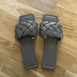 Flätade sandaler - Beige/gröna sandaler/tofflor i skinnimitation. Skorna är flätade och de har ingen klack. Aldrig använda, som nya.