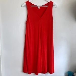 Orange A-linje kort klänning, stl 34 XS, basic, miniklänning, ärmlös, V-ringad - Orange klänning i A-linje modell utav viskostyg med tungt fall. Mått i cm: bröstvidd 41; axelbredd 31; längd från axeln 90.
