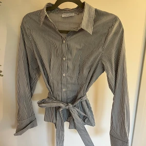 Randig skjorta med knytdetalj - En blå vit randig shorta från Lindex med en knytdetalj i midjan, använd två gånger utan defekter men kommer inte till användning, nypris 400kr. Vid fler frågor eller bilder är det bara att kontakta i chatten. Köparen står för frakten💕