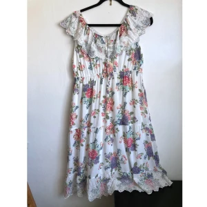 Vit blommig midiklänning, 42 M, romantisk, rosa, lila, spets, broderi, broderad, somrig, bohemisk - Vit midiklänning i luftig vävd viskos med blommor, virkade spetsdetaljer, knytband i ringningen, resår i midjan. Mått i cm: bröstvidd 49; längd fram från axeln 106.