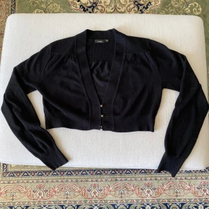 Svart stickad kofta  - Kort svart stickad kofta. Jättefint att ha över en topp eller som blus för sig. Knappt använd. Passar s