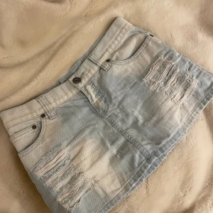 Jeanskjol - Cool jeanskjol med hål (syns ej igenom).  Midjemått tvärsöver: 40cm. Längd på kjolen: ca 28cm. Märke: Fishbone Pris går att diskuteras