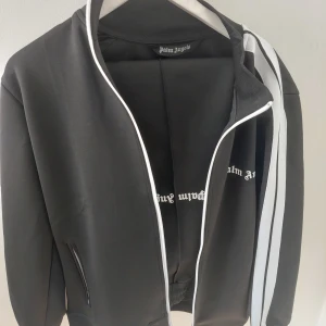 Palm Angels Tracksuit - Fin svart Palm Angels Tracksuit storlek M. Koftan använt cirka 5 gånger byxorna använt 1 gång. Säljer för att den inte passar mig. Osäker på autenticitet men QR-kod scannar!