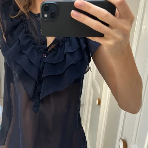 Mörkblå meshblus med volanger - Så fin mörkblå blus med volangdetaljer framtill! Knappt använd så mycket bra skick!