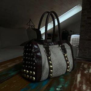 Väska - Väska med beige tyg och brunt läder. Både silver och guld knappar så enkelt att matcha smycken till🤎 defekt: liten fläck på fodret i insidan.