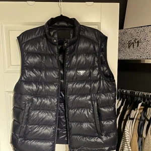 Prada Nylon Väst - Säljer nu min Prada väst då den inte kommer till användning längre. En mindre skada på utsidan av fickan och ett litet hål innanför högerfickan men inget som syns! Storlek: 54, sitter som en M/L Färg: mörkblå Skick: 7/10 Nypris: 14000kr