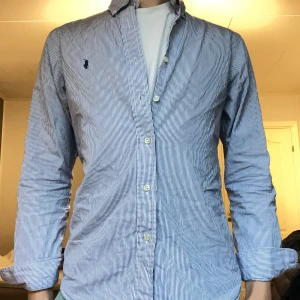 Ralph Lauren skjorta blå vit randig - Säljer en jätte schysst skjorta från Ralph Lauren som är i storlek S i slim fit. Den är i otroligt bra skick enbart att den har hängt i garderoben ett tag så den är behöver bli strykas lite men annars är den otroligt bra skick.