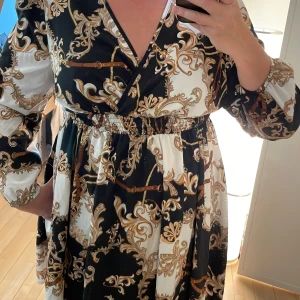 Elegant klänning, lång blus - Elegant mönstrad klänning. Resår i midjan o v-ringad fram. Lång ärm med resår nedtill. Svalt material 