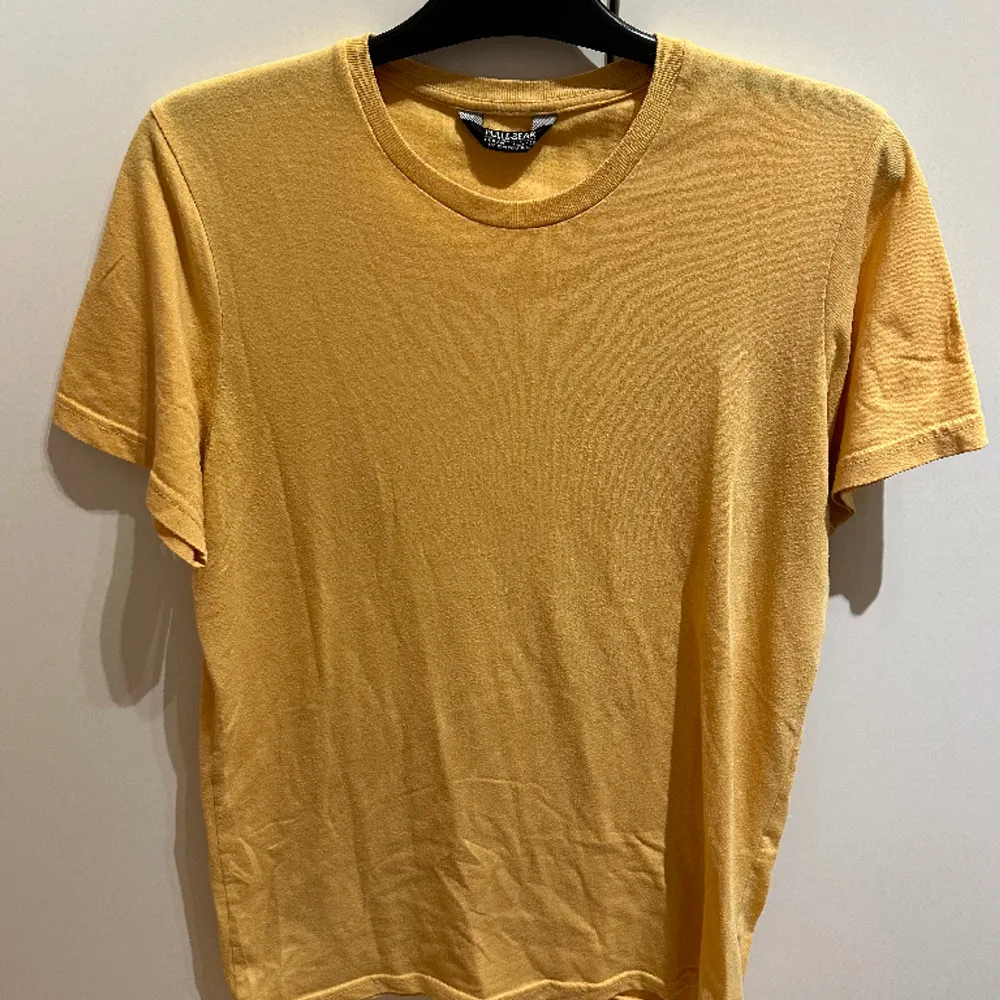 Säljer en mörkgul t-shirt från Pull&Bear med lätt passform. Den är ganska oanvänd och är i bra skick men lite urtvättad. . T-shirts.