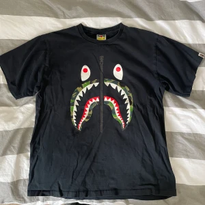 Bape Shark T-shirt  - Bape T-shirt i använt skick! Designen krackelerad och litet hål på framsidan, Storlek XL men passar M/L
