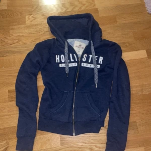 Mörkblå Hollister kofta - Super snygg Hollister kofta i mörkblå med tryck på framsida. Mysigt material på innersidan vilket ger tröjan skön men samtidigt snygg. Pris kan diskuteras😊
