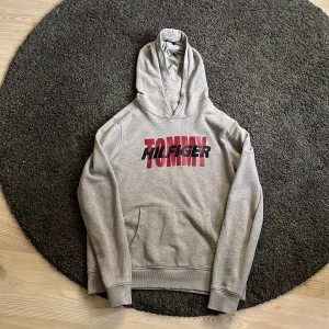 Tommy Hilfiger hoodie - En grå hoodie från Tommy Hilfiger. Köptes på kidsbrandstore för 900 kr. Finns små defekter men tröjan är i stort i bra skick. Dessa man se på bilderna! Storleken är 176 men den sitter som S.  För fler bilder är det bara att fråga! 