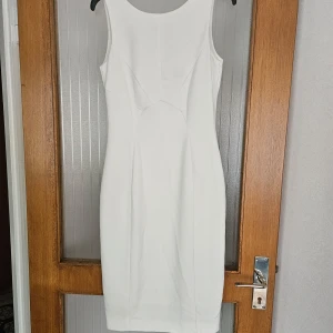 Vit klänning från H&M - En elegant krämvit klänning från H&M med ärmlös design och en dragkedja på baksidan. Klänningen har en figurnära passform och är knälång. Aldrig använd.  Passar bättre till storlek S-M