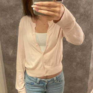 Ljusrosa kofta från H&M - En ljusrosa kofta från H&M med knappar framtill. Koftan har långa ärmar och ribbstickade muddar vid ärmslut och nederkant. Använd 2 gånger, inga slitningar.