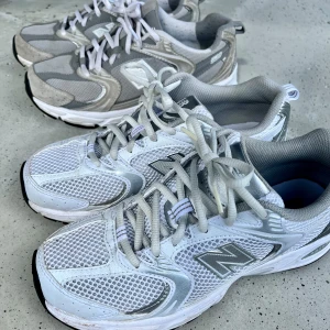 New Balance sneakers i vitt och grått - Ett par New Balance sneakers i vitt och grått. Skorna har en mesh- och syntetisk ovandel med snörning. De har en bekväm sula som är idealisk för träning och vardagsbruk.