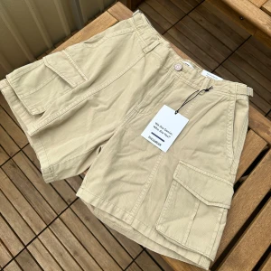 Beige cargo shorts från Pull&Bear  - Aldrig använda! Shortsen har justerbara band i midjan. Sitter som storlek w28 i midjan men man kan spänna in shortsen så att de sitter som w26. Sista bilden är tagen från deras hemsida där man ser hur de sitter på.