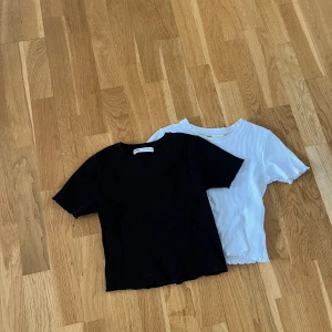 Två st t-shirt - Två likadana tröjor i svart och vit. Ribbat material. Tröjorna sitter tajt och är kortare men ändå längre än en vanmig magtröja. Hyfsat välanvända men ändå bra skick fortfarande. 