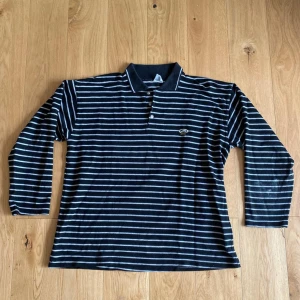 Svart och vit randig pikétröja - En svart och vit randig pikétröja med långa ärmar. Tröjan har en krage och knappar vid halsen. Fett skön