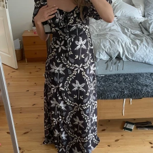 Maxi Klänning - Svart Maxiklänning med vita blommor, köpt på Sellpy! Klänningen har även en snygg slits. Aldrig använd (en av lapparna kvar som syns på bilden) Säljs då den tyvärr är lite för stor för mig. Pris kan diskuteras🌼🌼
