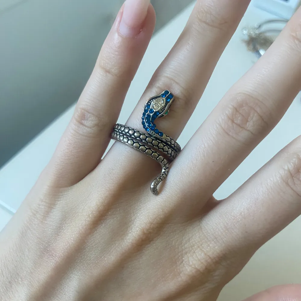 En unik ormformad ring i silver med blå detaljer. Ringen är designad för att slingra sig runt fingret och har en realistisk ormskinnsstruktur.. Accessoarer.