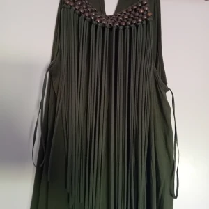 Grön långklänning från Zara Basic - En elegant grön långklänning från Zara Basic med dekorativa pärlor och fransar vid halsringningen. Klänningen har en öppen rygg och tunna axelband.