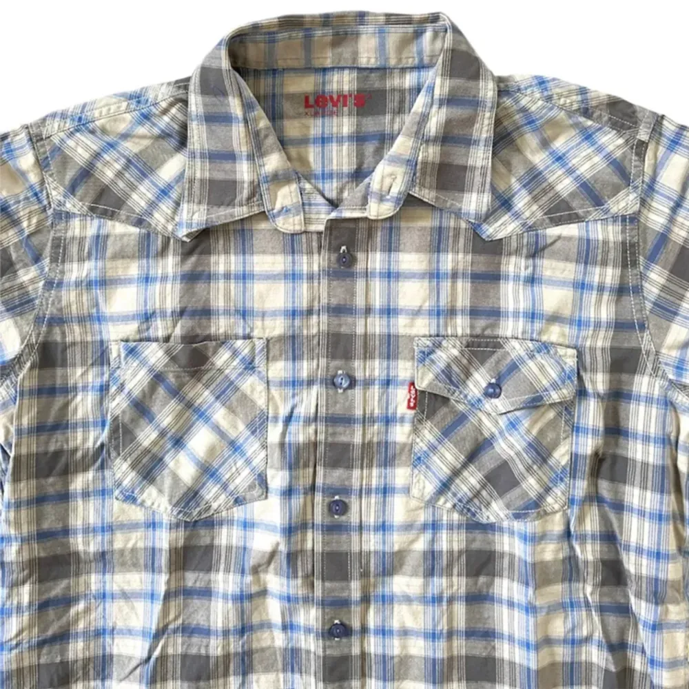 Kortärmad levis skjorta med blått rutigt mönster. Inga funktionella defekter. Storlek XL på taggen men har klippt av den så den sitter mer som en bred M/L. Väldigt snygg med en långärmad tröja under. Skriv för mått eller frågor!. Skjortor.