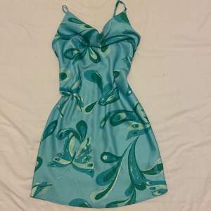 Grön silkes klänning med turkosa mönster från Urban outfitters. Nu pris 599. Den har som en ”häng krage” där uppe. Perfekt till sommaren. Helt oanvänd.
