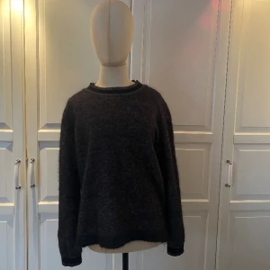 Stickad tröja  - En stickad svart långärmad tröja med trendiga krag- och arm detaljer. Material: 60% Super kid mohair, 36% nylon och 4% spandex. Denna otroligt mjuka och gosiga tröja är i gott skick, och skulle passa snyggt med en svart tjol eller kostymbyxor💘