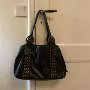Svart handväska  - Säljer denna superfina svarta handväska med nitar. Den har tre stora fack med dragkedja.