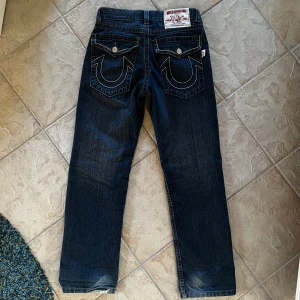 True Religion jeans, Bobby - Hej! Säljer nu ett par True Religion jeans som tyvärr var för små för mig när jag köpte dom. Är lite slitna där nere. Mått; Midjemått: 29cm, Ytterbenslängd: 104cm, Innerbenslängd:72cm, Benöppning: 21cm  Hör av dig vid frågor!