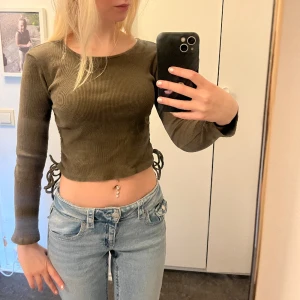 Grön tröja/topp - Grön croppad tröja med band på sidorna. Snygg men använder aldrig och den sitter bra på. Den är stretchig och tror den kan passa folk mellan S-M