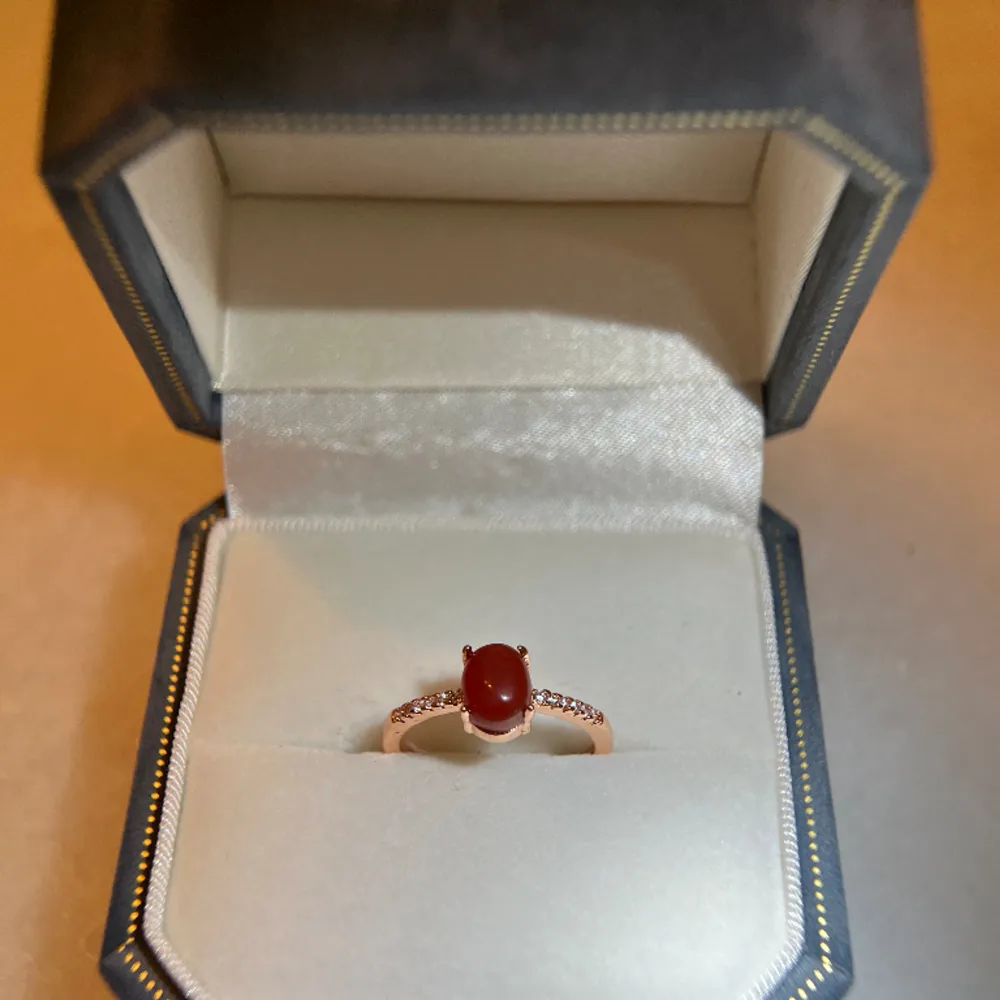 The ring is made of S925 silver with tag on it. Rose gold plated, genuine red jade, besides it are zircons. The Ring is adjustable size. Brand new, with jewellery bag provided . Accessoarer.