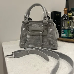 JÄTTEFIN VÄSKA!! - Säljer denna jätte coola ljusgråa mini väska med silver nitar på. Köpte den på sellpy. Man får me snören som man kan sätta på och ta av väskan. Passar till många olika outfits!!