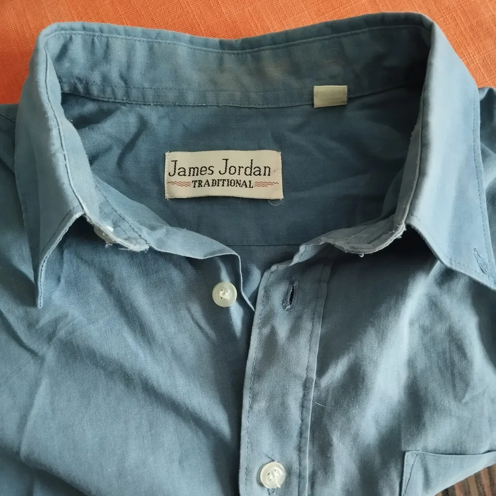 Blå skjorta från märket James Jordan traditional. Material; 60% bomull och 40% polyester. Finns två extra knappar på insidan. Lite smutsig på insidan av kragen. Pressveck på ryggen.. Skjortor.