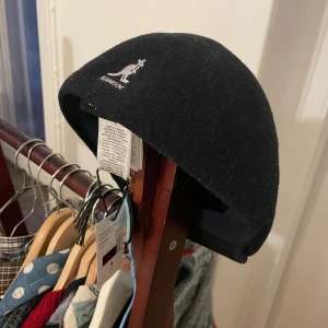 Kangol  - Äkta Kangolkeps i storlek S i en marinblå färg. Inköpt på hattbaren i NK för kanske ett år sedan. Lapp kvar å helt oanvänd.