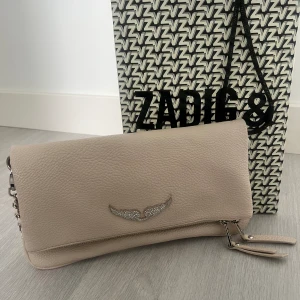 Zadig väska - Säljer nu min beiga Zadig väska då den inte längre kommer till användning. Endast använd en kort period så väskan är i toppskick, inga defekter. Långt och kortband följer me  Fler bilder kan fås. Äktighetsbevis finns.  Nypris 2800 kr Mitt pris 750 kr