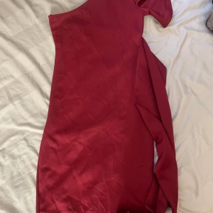 One shoulder vinröd midi klänning från boohoo - En festlig one shoulder vinröd midi klänning från boohoo med jersey tyg och fastspänt bälte. One shouldern har även en volang. Är ej använd men lite lösa stygn vid axeln.