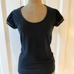 Svart topp från Burberry - Säljer en söt svart topp från Burberry i storlek M. Toppen har korta ärmar med fint rynk med Burberrys ruta som detalj. Rund halsringning och en lagom tight passform. Den är tillverkad i skön trikå, perfekt för både vardag och fest!🖤