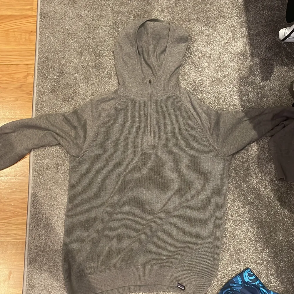 Säljer en grå hoodie från Patagonia. Den är supermysig och perfekt för kyliga dagar. Hoodien har en halv dragkedja framtill och är tillverkad i ett stickat material. Den har långa ärmar och en normal passform. Perfekt för höst och vinter!. Tröjor & Koftor.