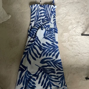 Blåvit långklänning från H&M - Säljer en superfin blåvit långklänning från H&M. Klänningen har ett snyggt bladmönster och är perfekt för sommaren. Funkar även som lång kjol och passar parfekt med en gullig topp. Den är ärmlös och har smala axelband. Materialet känns lätt och luftigt, vilket gör den idealisk för varma dagar. Perfekt för både vardag och fest! 